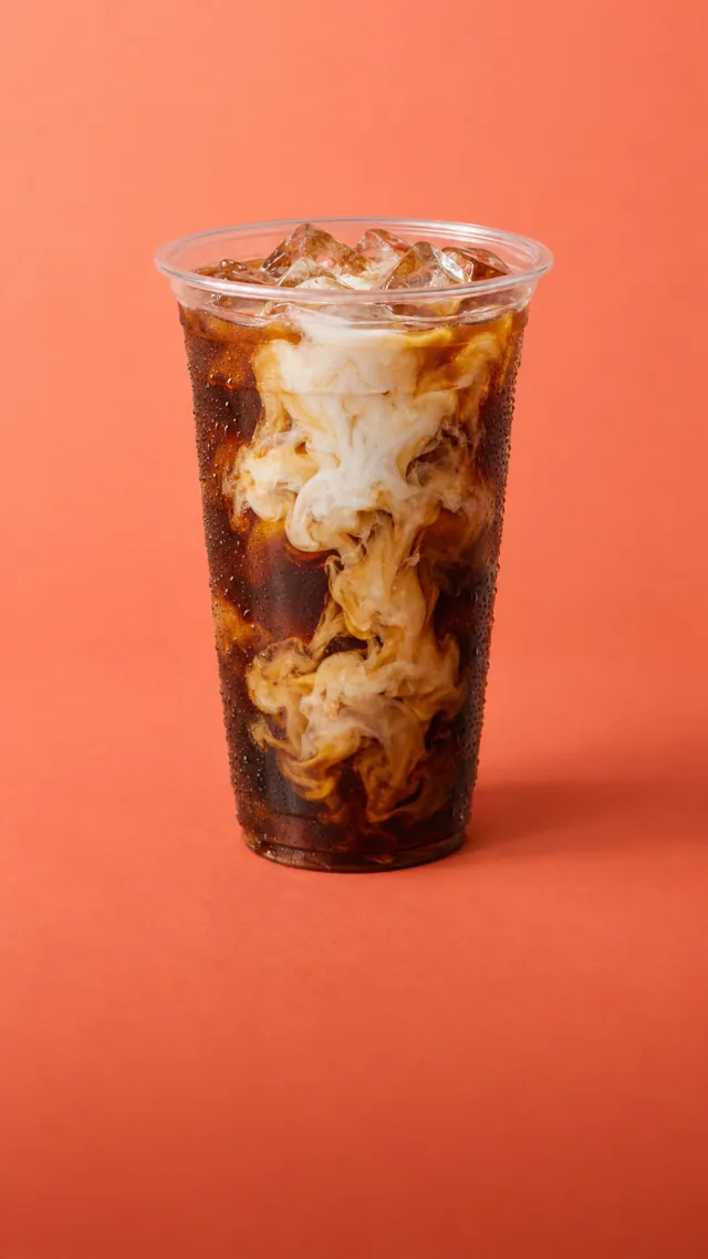 Cream swirling into iced cold brew in a clear cup